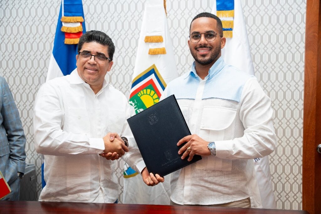 El rector del ITLA, Rafael Féliz García, y el alcalde de Santo Domingo Este, Dio Astacio, estrechan la mano tras firmar un convenio interinstitucional, acompañados por autoridades de ambas instituciones.